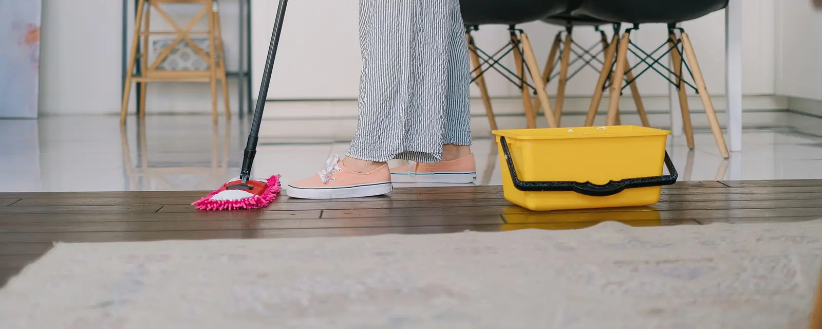 Mopping a wooden floor at home next to a yellow bucket